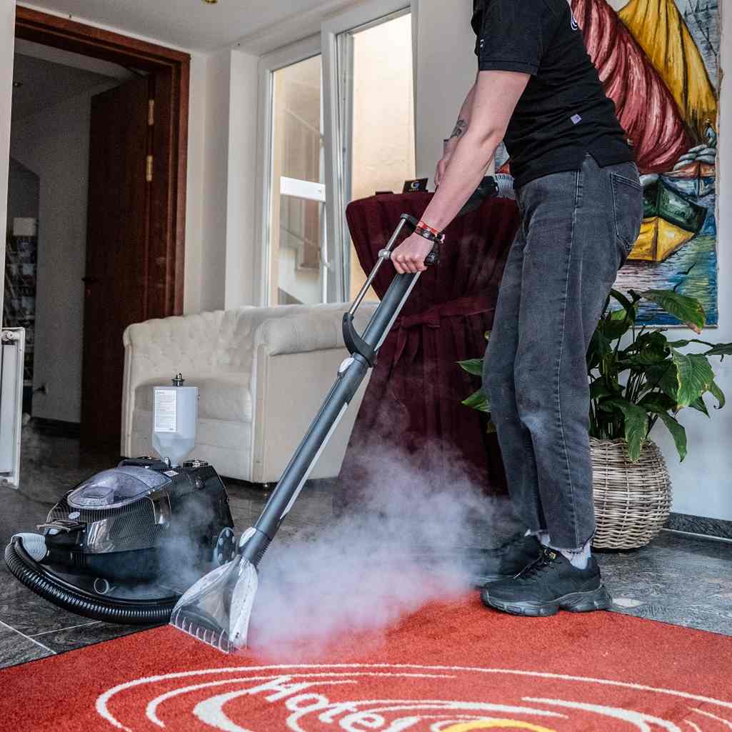 Reinigungskraft reinigt mit Dampfreiniger Teppichboden.